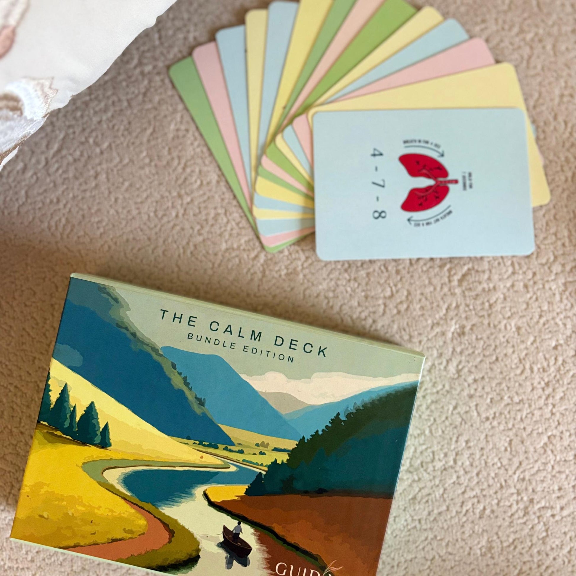 The Calm Deck Bundle Edition by Guiding Koi placed beside a spread of colorful mindfulness cards - a 30-card psychologist-designed tool to manage anxiety and build calm.