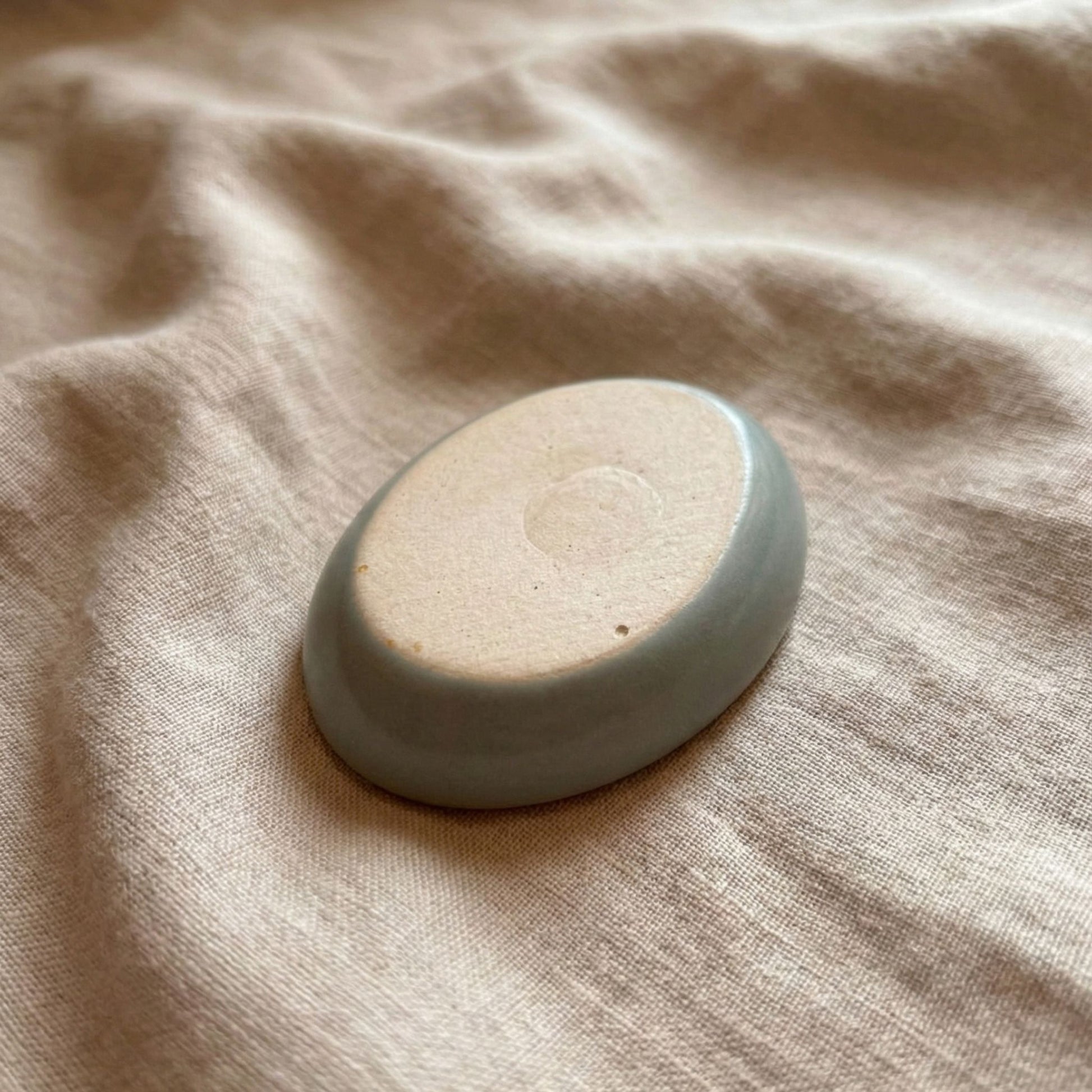 Backside view of a handmade ceramic worry stone with a smooth matte base placed on soft beige fabric, used for grounding, anxiety relief, and soothing tactile support.