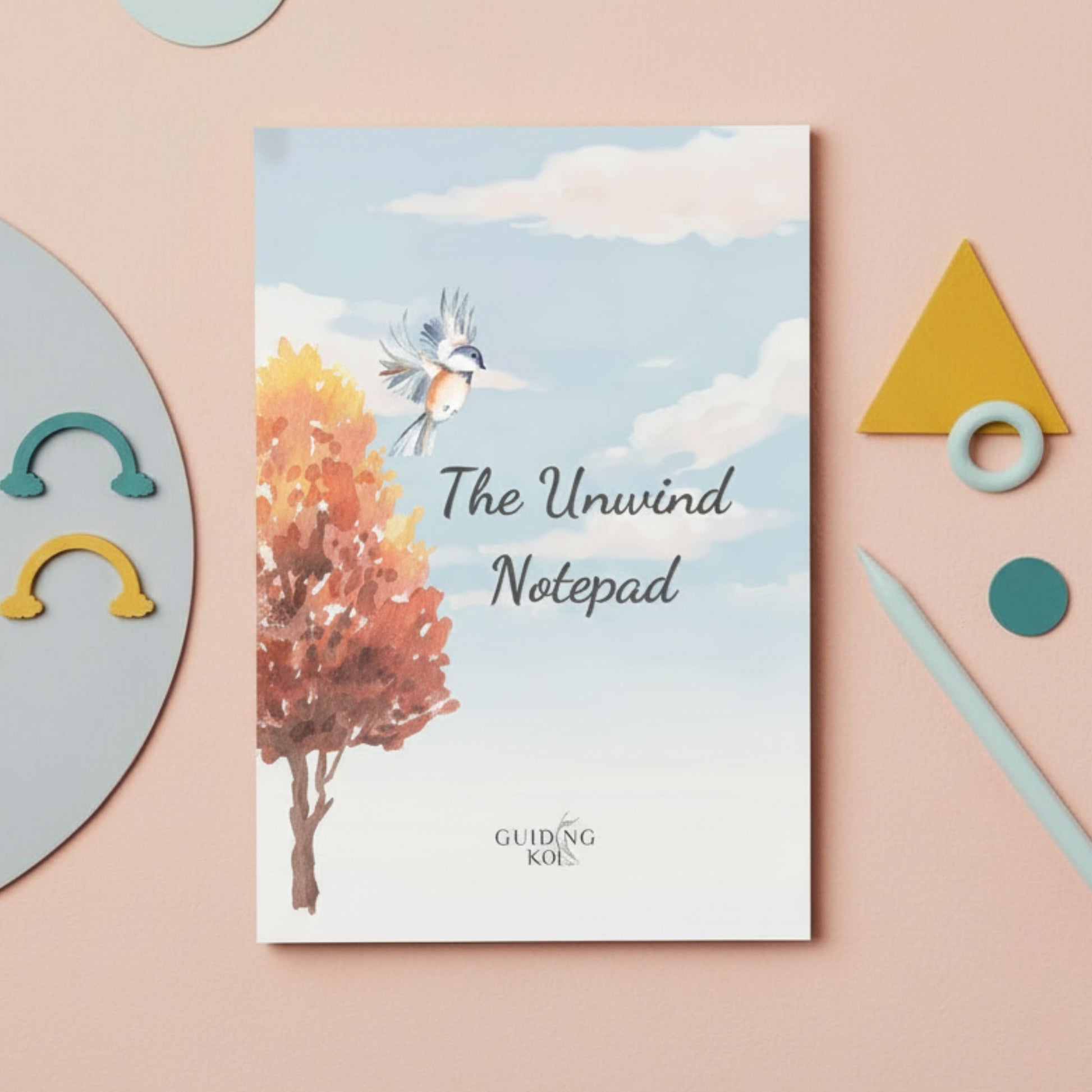 Guiding Koi Unwind Notepad placed on a pastel desk with playful stationery, featuring a calming illustration of a bird and autumn tree. A mindfulness notepad designed for stress relief, evening reflection, and unwinding after a long day.